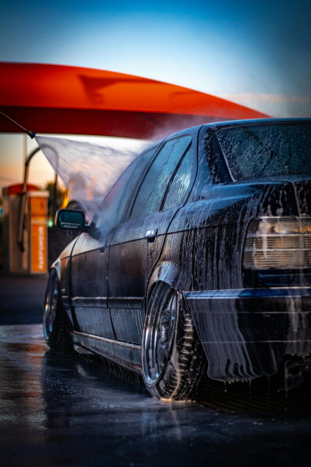 BMW E36 sedan being pressure-washed at sunset