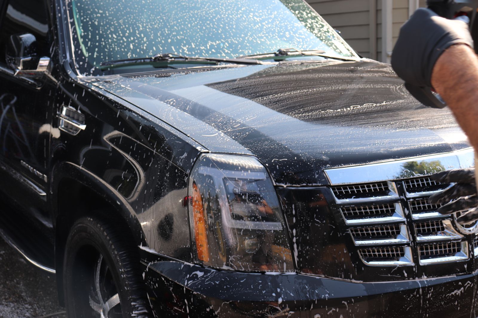 Foam covering the hood and windshield of a black Cadillac Escalade during the wash stage