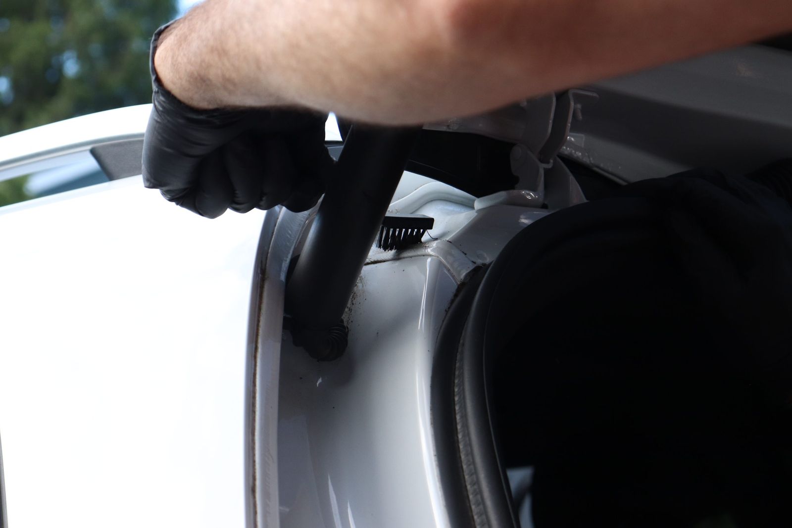 Detailer using a detail brush to clean the hood hinge and engine bay edge of a vehicle in a Bellevue driveway