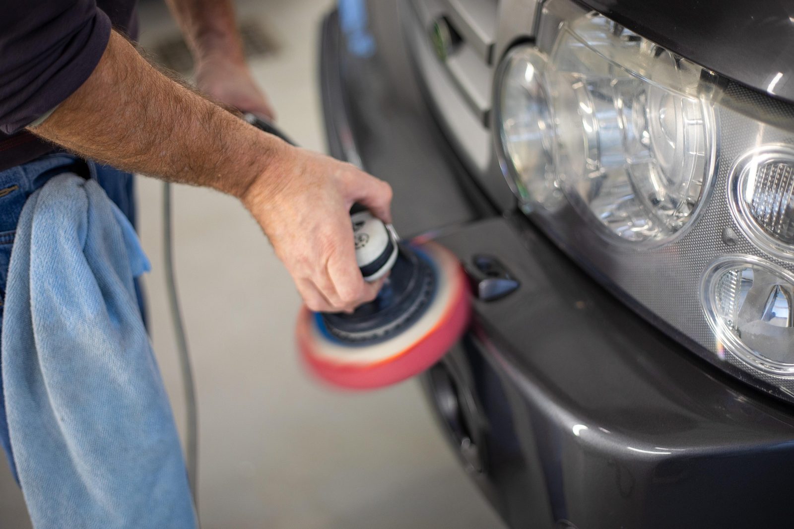 Polisher buffing the front of a dark vehicle