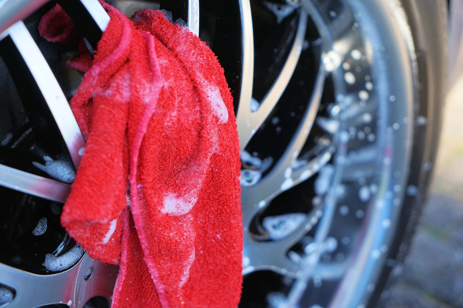 Red microfiber cloth on a chrome wheel covered in suds